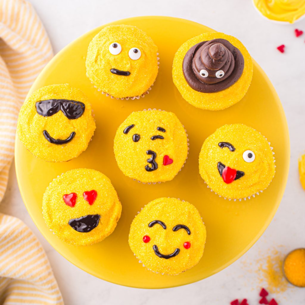 Yellow plate with emoji face cupcakes. 