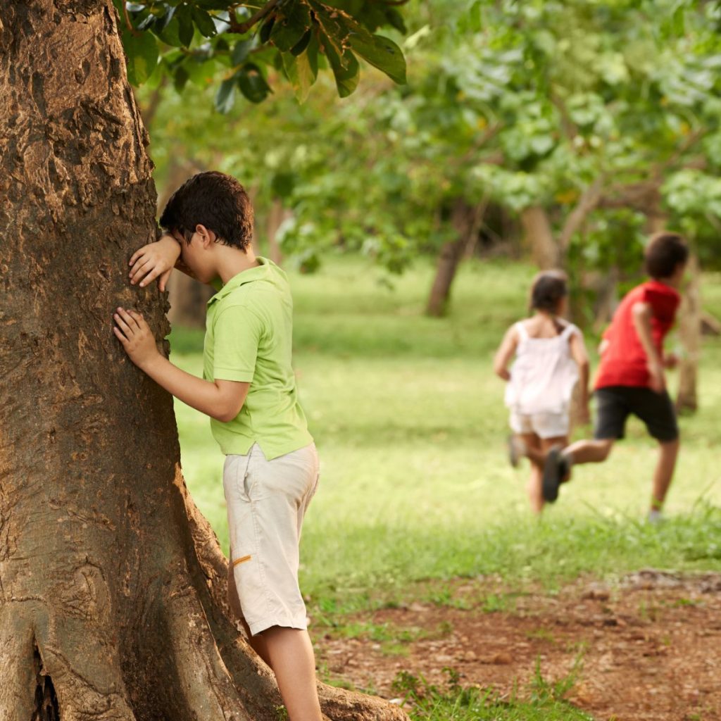 Kid counting by a tree with other kids running away.