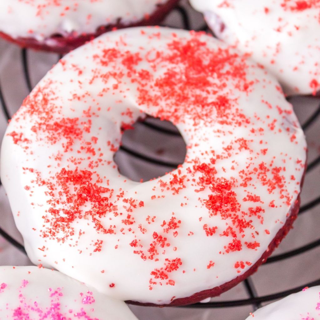 Donut on wire rack with white frosting and red sprinkles. 