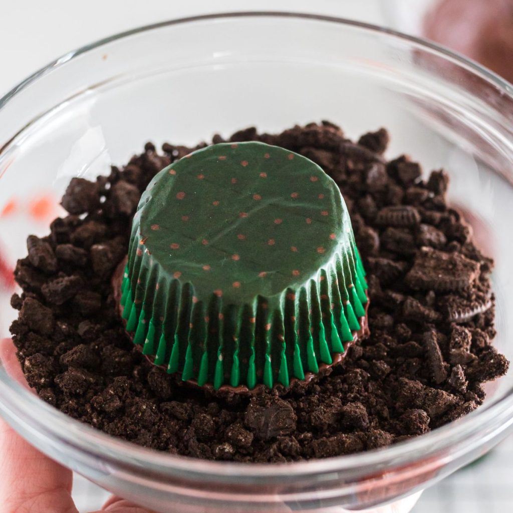 Cupcake being dipped in a bowl of chocolate cookie crumbs.