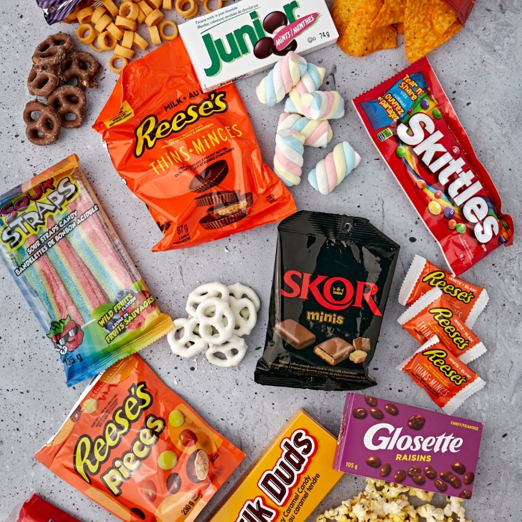 A variety of candy like skittles, Reeces, Milk Duds and chips. 