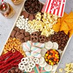 A tray with popcorn, candy, chocolate covered pretzels, and chips.