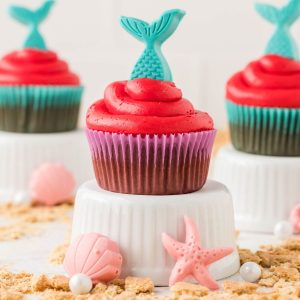 Chocolate cupcakes with red frosting and blue mermaid tail toppers.
