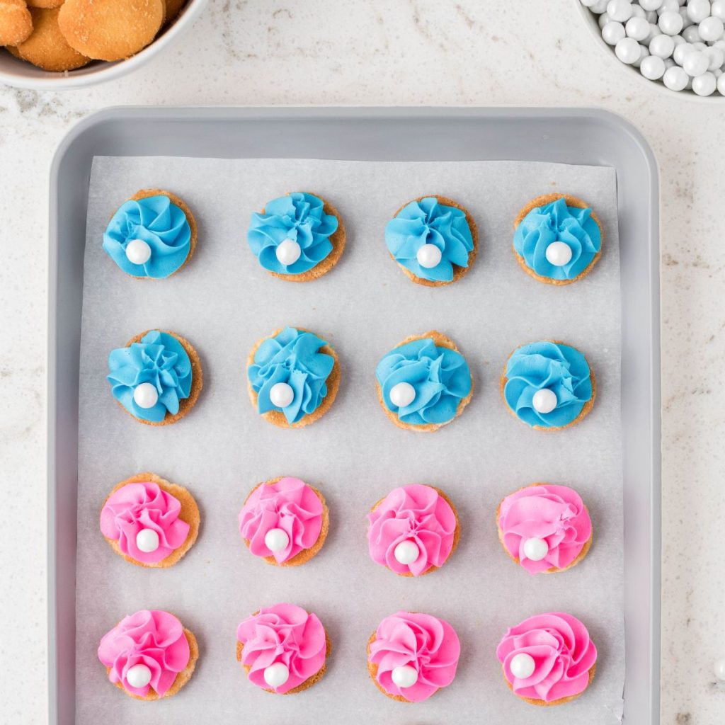 Vanilla wafers topped with blue and pink frosting and a white candy.
