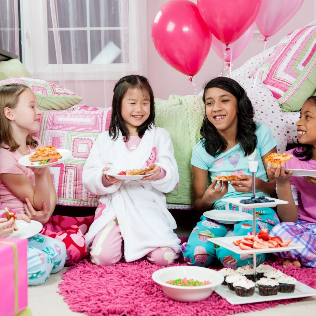 Girls in a bedroom with party food and balloons.