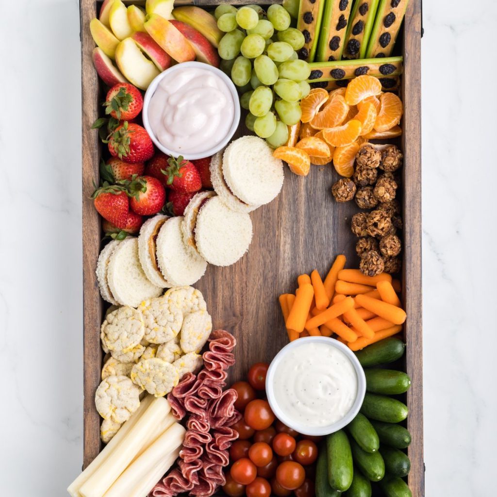 Board with fruit, vegetables, bowls of dip. 