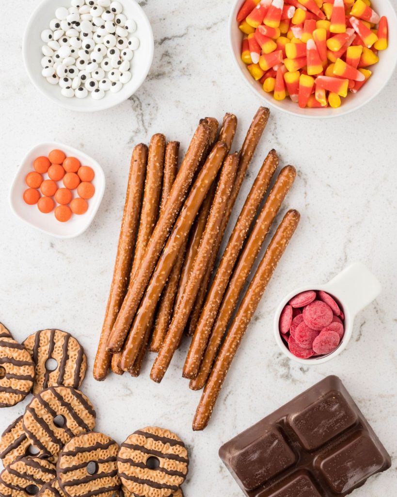 Pretzel rods, bowl of candy corn, candy eyes, and striped cookies. 