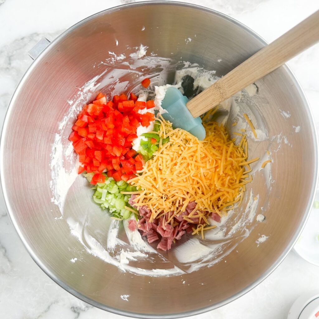 Mixing bowl with cream cheese, shredded cheese, and vegetables.