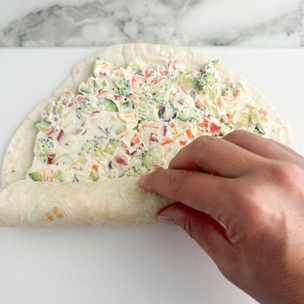 Tortilla with cream cheese vegetable mixture getting rolled up.