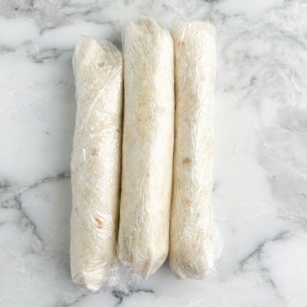 Three tortilla roll ups in plastic wrap.