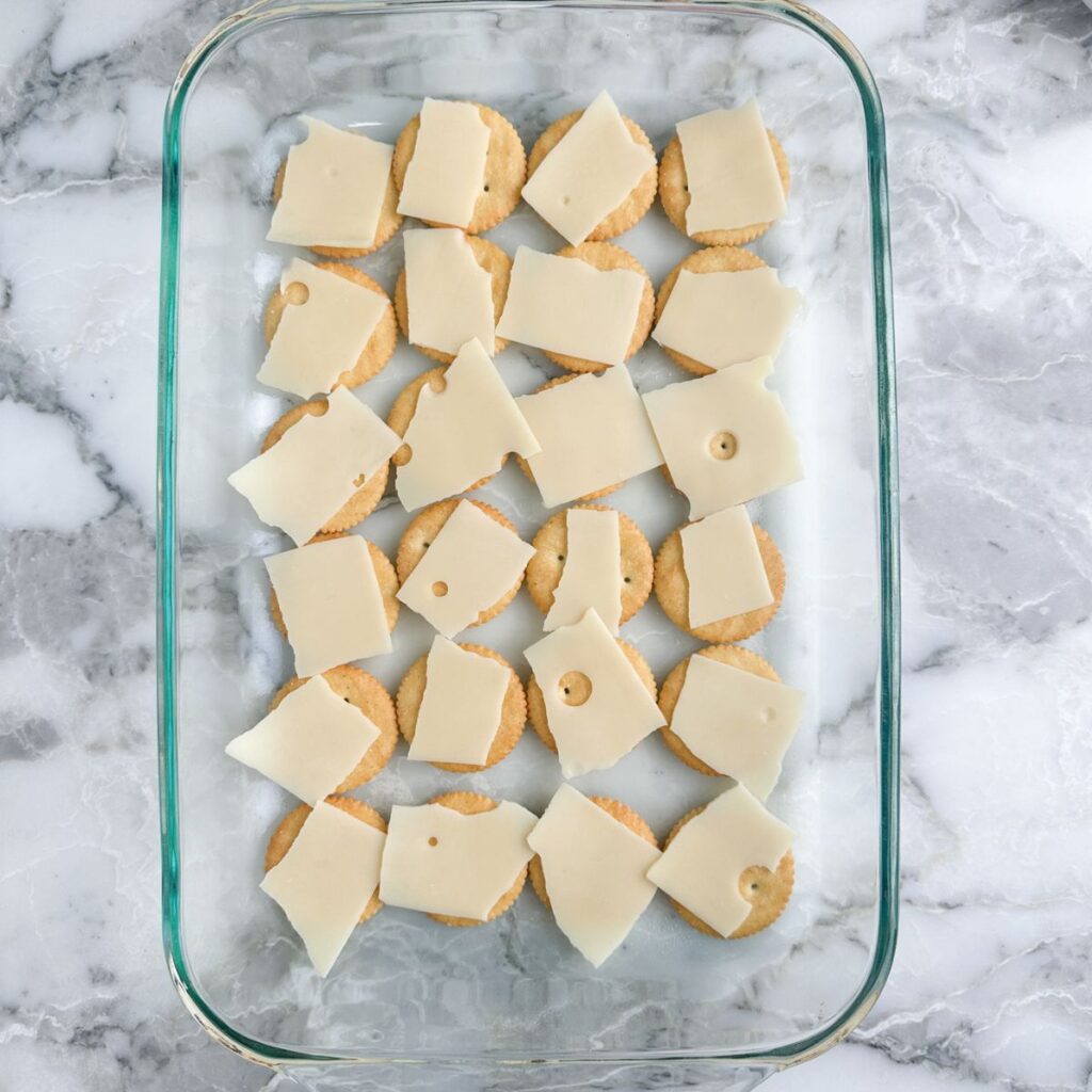 Baking dish with Ritz crackers topped with pieces of Swiss cheese.
