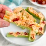 Hand holding celery stick stuffed with cream cheese mixture.
