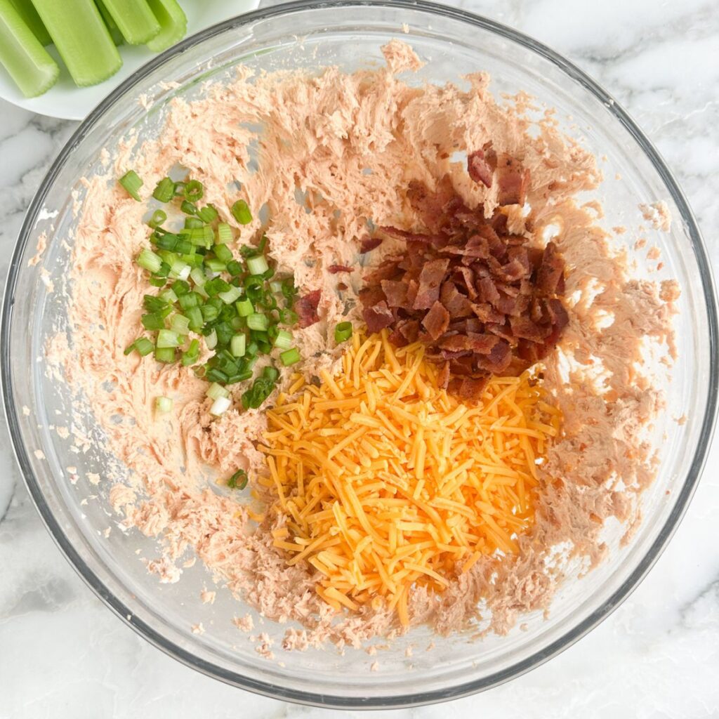 Bowl of seasoned cream cheese, shredded cheese, crumbled bacon, and green onions. 