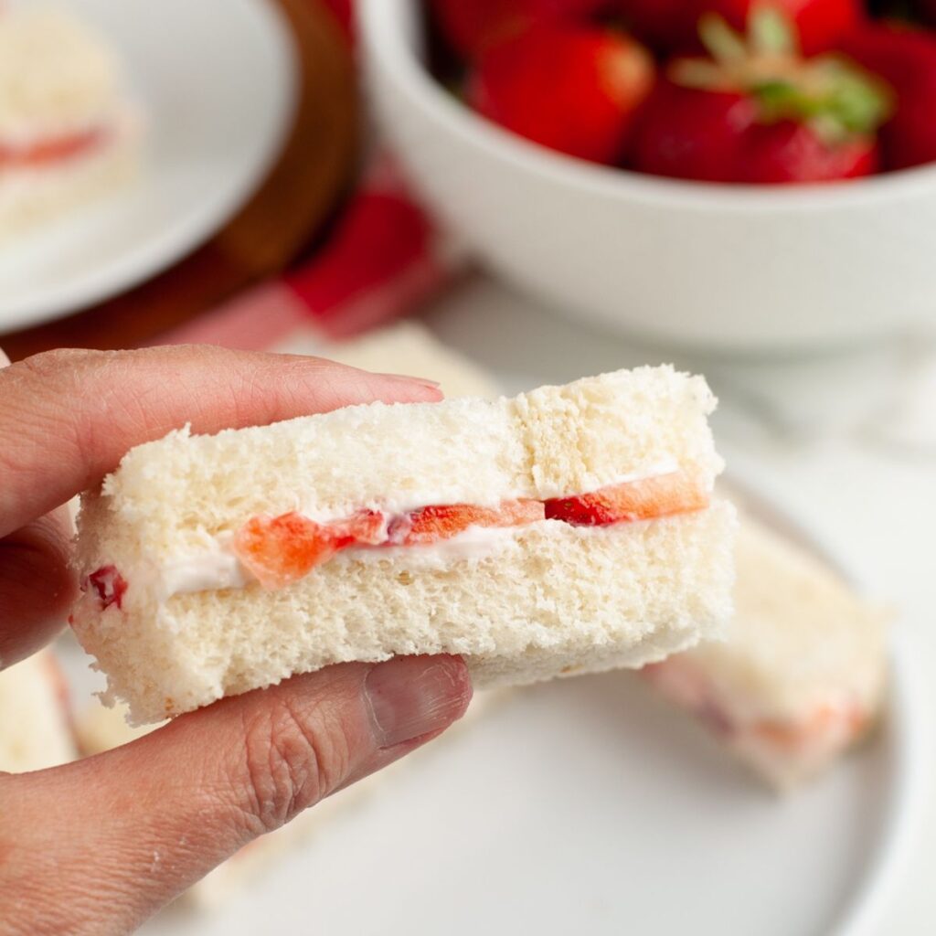 Hand holding a strawberry tea sandwich. 
