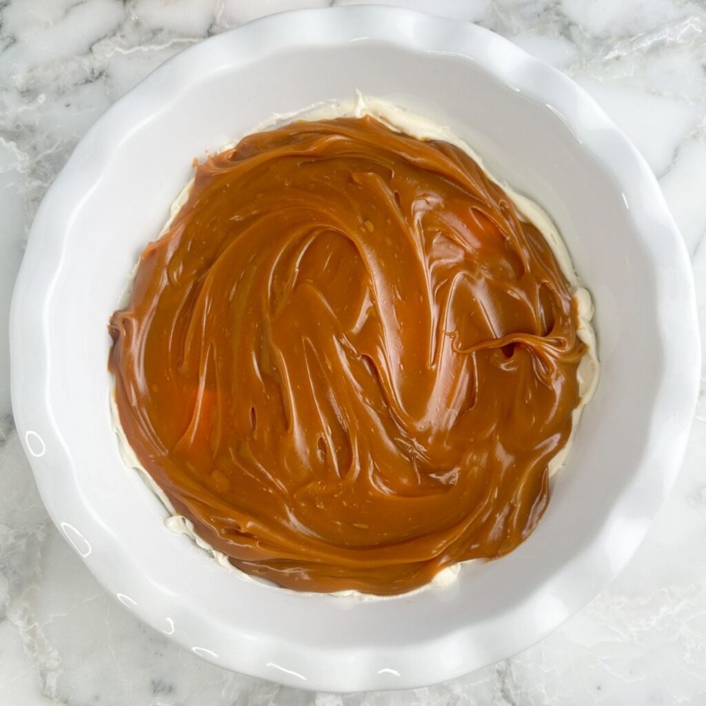 Pie dish with cream cheese and caramel dip spread in the dish.