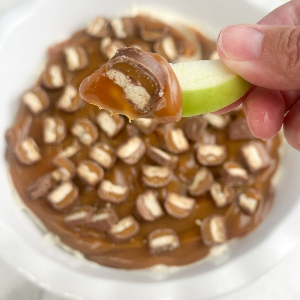 Hand holding a sliced apple with Twix Dip on it. 